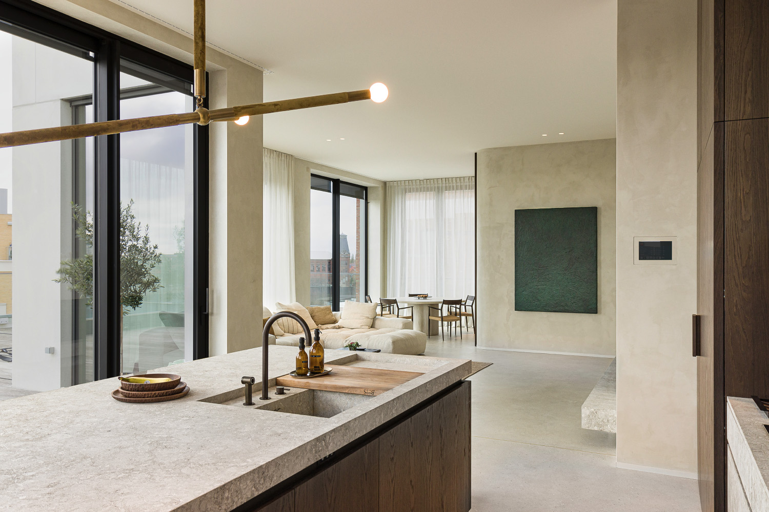 Kitchen island with stone surface, sink, soap dispensers, sectional sofa, dining table, and large windows.