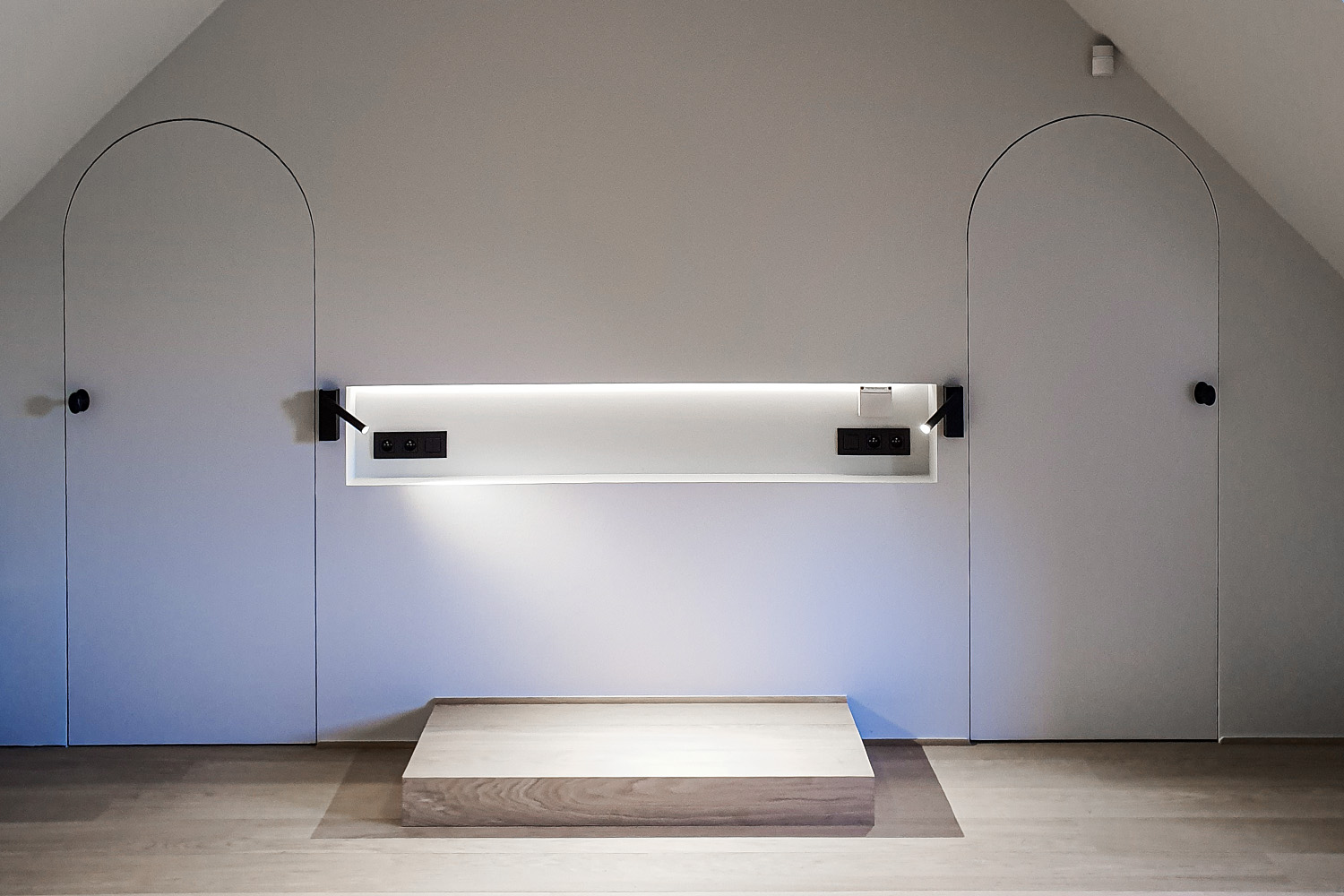 Symmetrical wall with two arched doors, recessed shelf with lighting and outlets, and raised wooden platform.