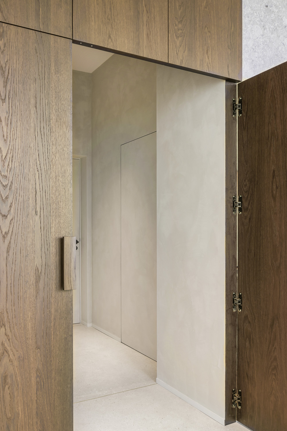 Interior with partially open wooden door, hallway with concealed panel, and overhead wooden cabinets.