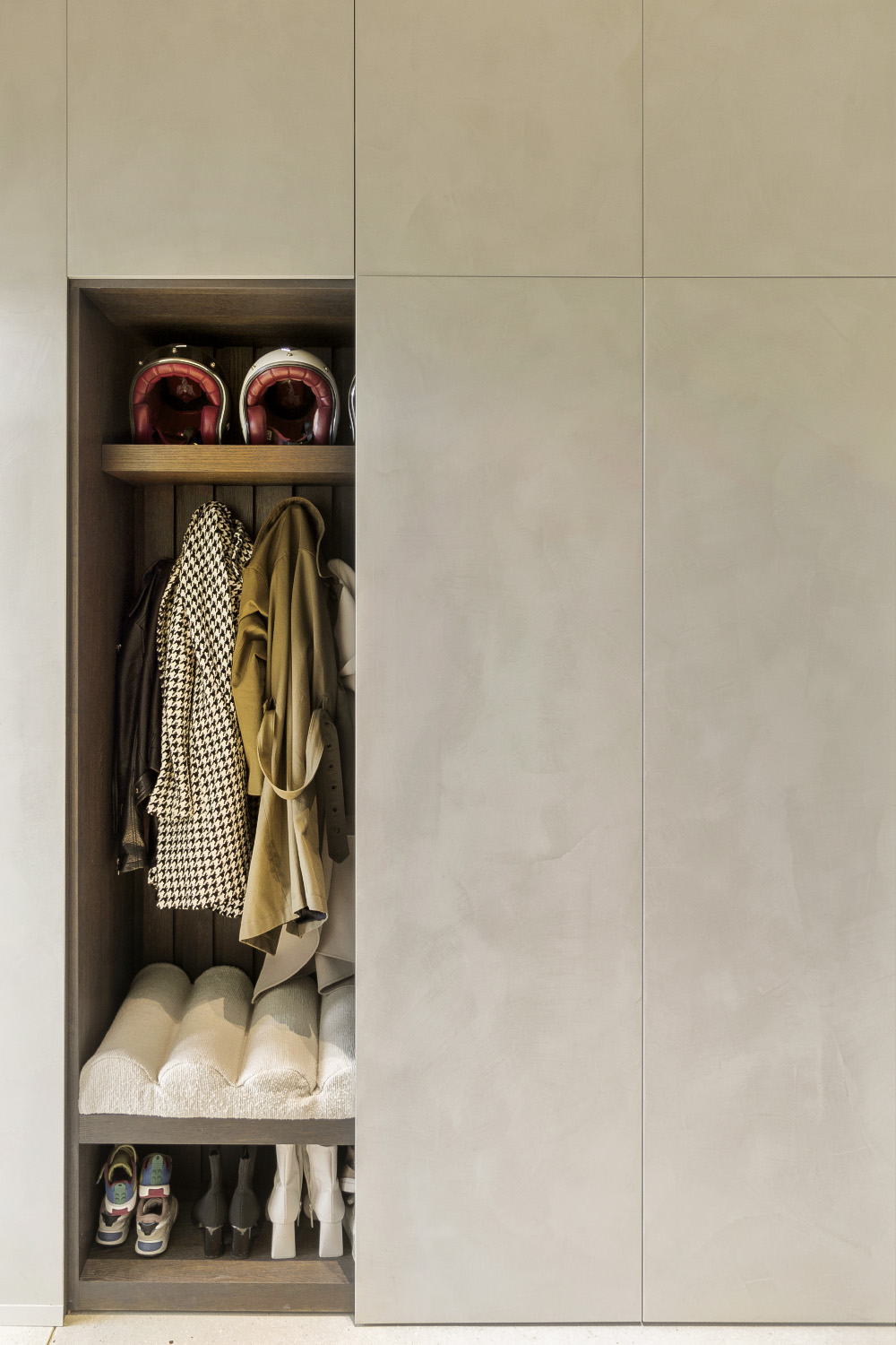 Open built‑in wardrobe with helmets on top shelf, coats on hooks, cushioned bench, and shoe rack.